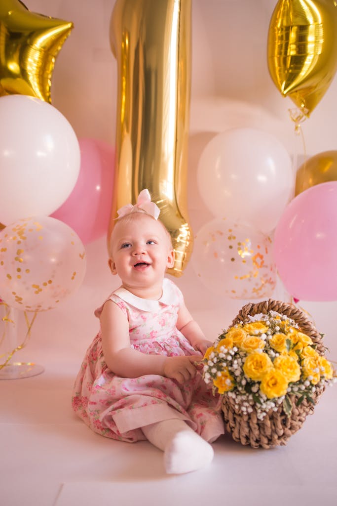 first birthday Baby Girl in Pink Dress Sitting on Floor with Basket of Flowers and birthday balloons